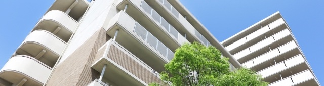 一棟のきれいなマンションと緑と青空の写真